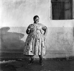 A woman beams as she poses against a wall, a hand on her hip.