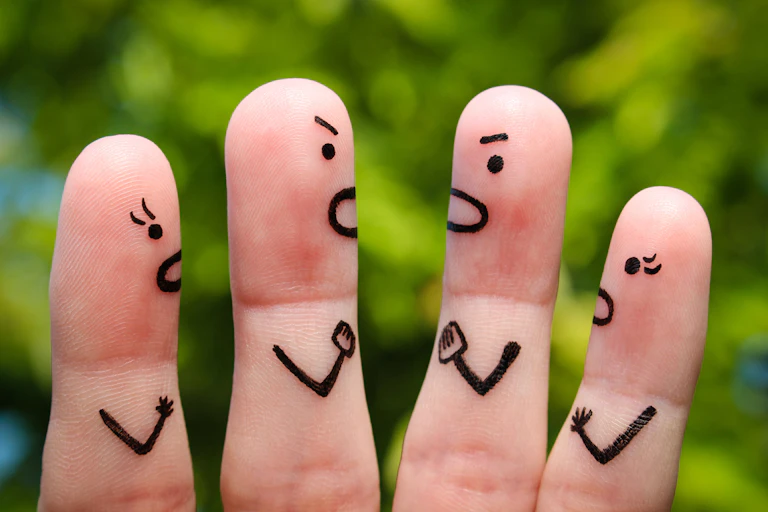 Four fingers with angry faces and arms drawn on them to look like two teams of two shouting at each other