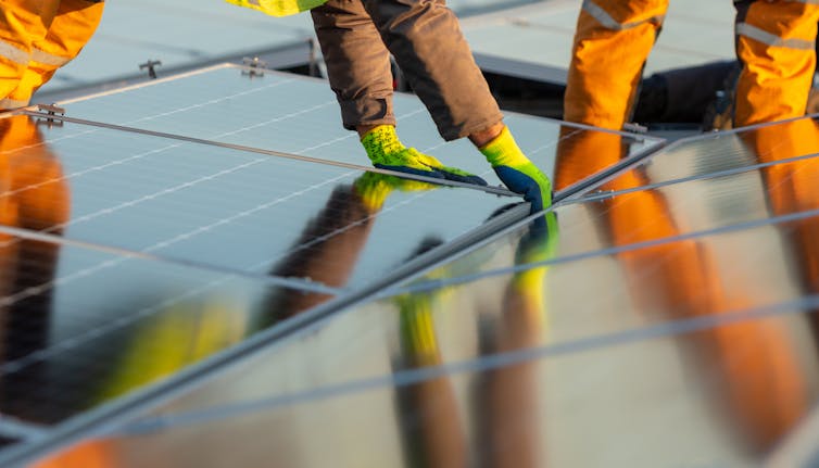 Hands lowering solar panels into place on a roof.