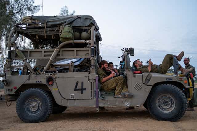 People rest in the seats and on the hood of a military vehicle.