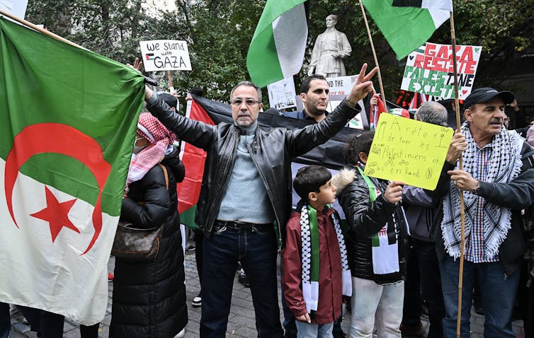 A man holds an Algerian flag in front of a crowd carrying placards