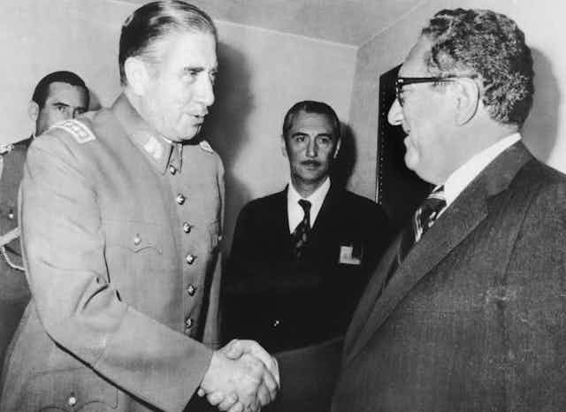 Man with mustache shakes Kissinger's hand