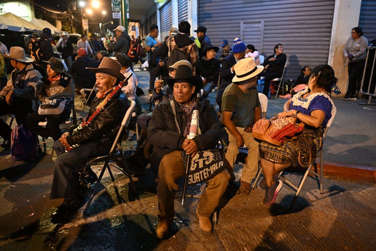 Indigenous men and women sit in chairs on street at protest