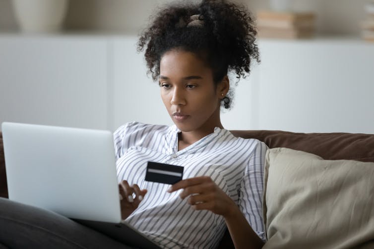 A woman looks at her computer while holding a credit card.