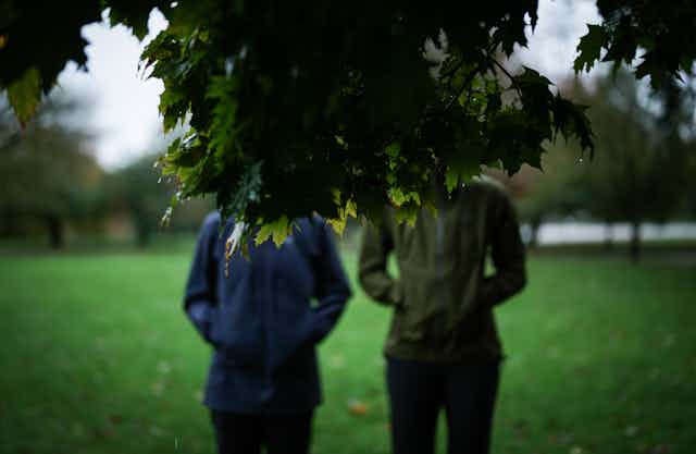 Two women facing away from the camera standing in a park. 