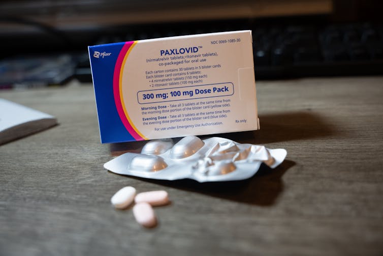 A box of Paxlovid, blister pack and some pills on a surface.