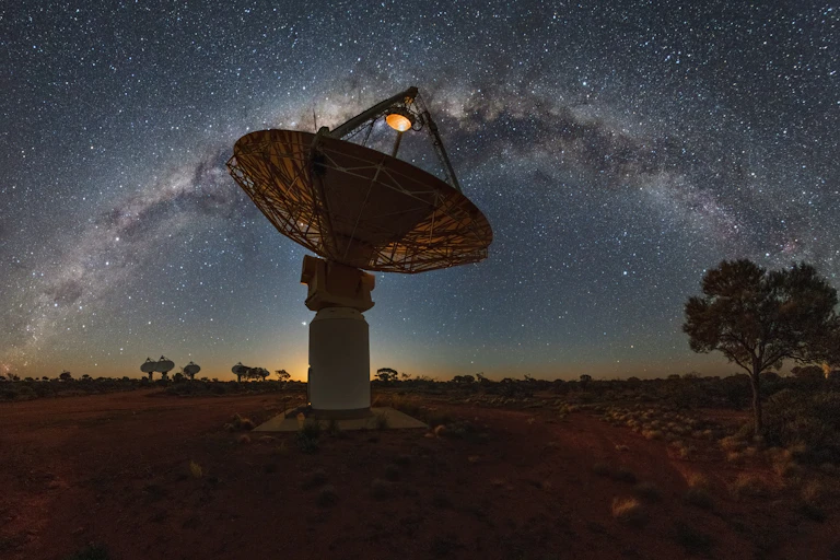 A large radio telescope silhouetted against the milky way in the night sky