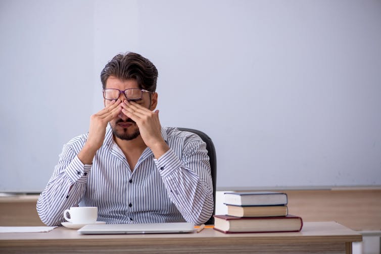 A teacher rubs his eyes while looking tired.