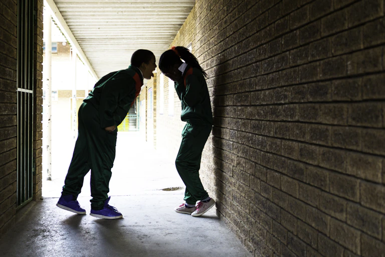A school boy screams in a school girl's face, as she covers her face with her hands.