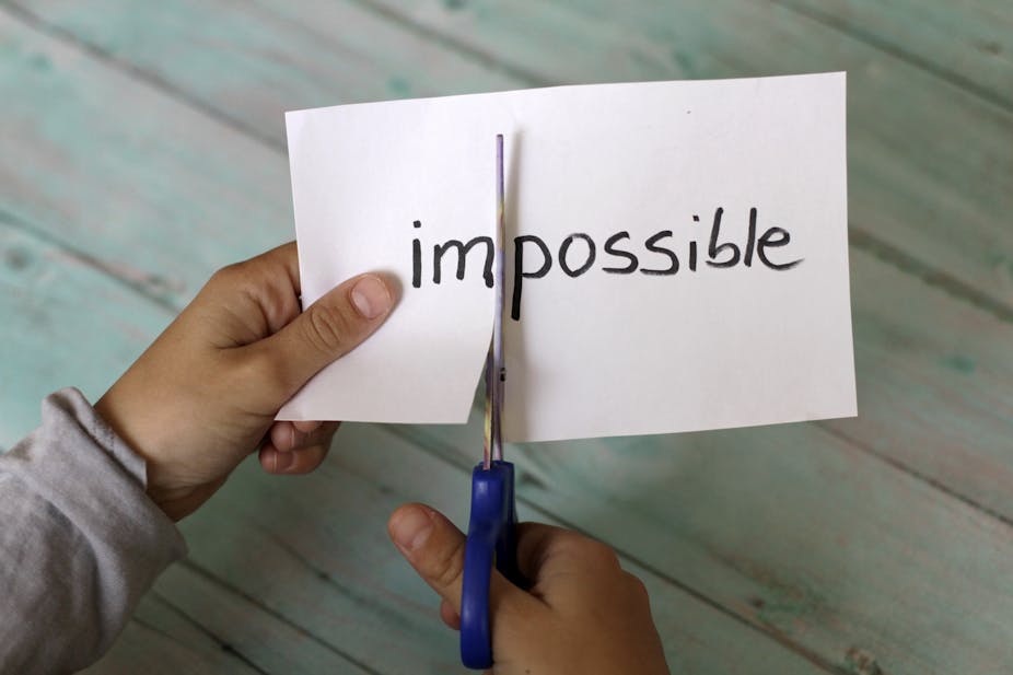 Hands holding paper and scissors. The word 'impossible' on the paper is being cut into 'im' and 'possible'.