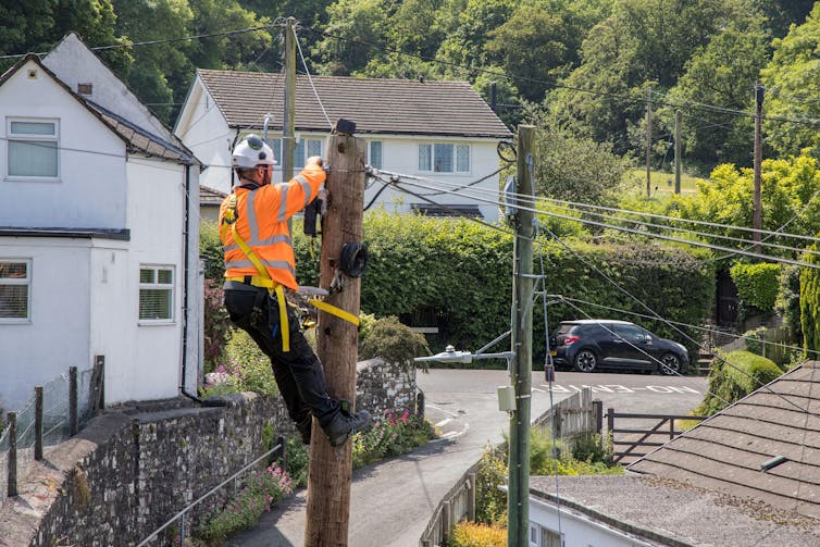 An engineer in a hard hat up a telephone pole installing fibre optic cable