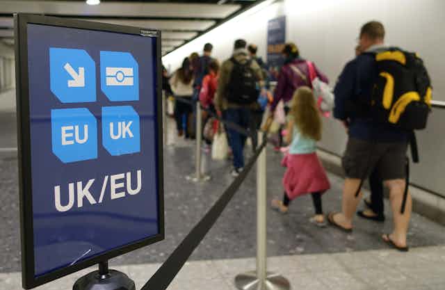 Photo of a family in an immigration queue at an airport, next to a sign indicating UK and EU passports