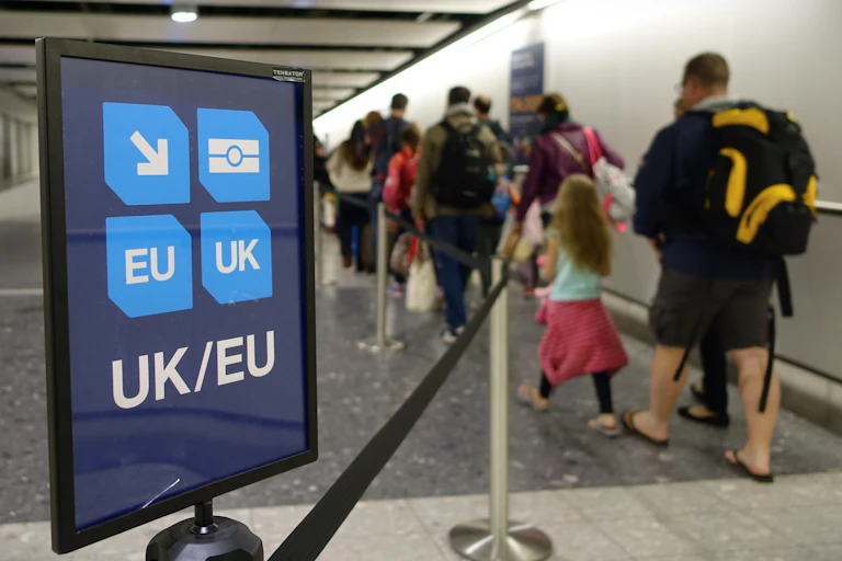 Photo of a family in an immigration queue at an airport, next to a sign indicating UK and EU passports