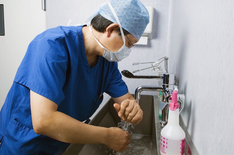 masked man in scrubs washing at sink