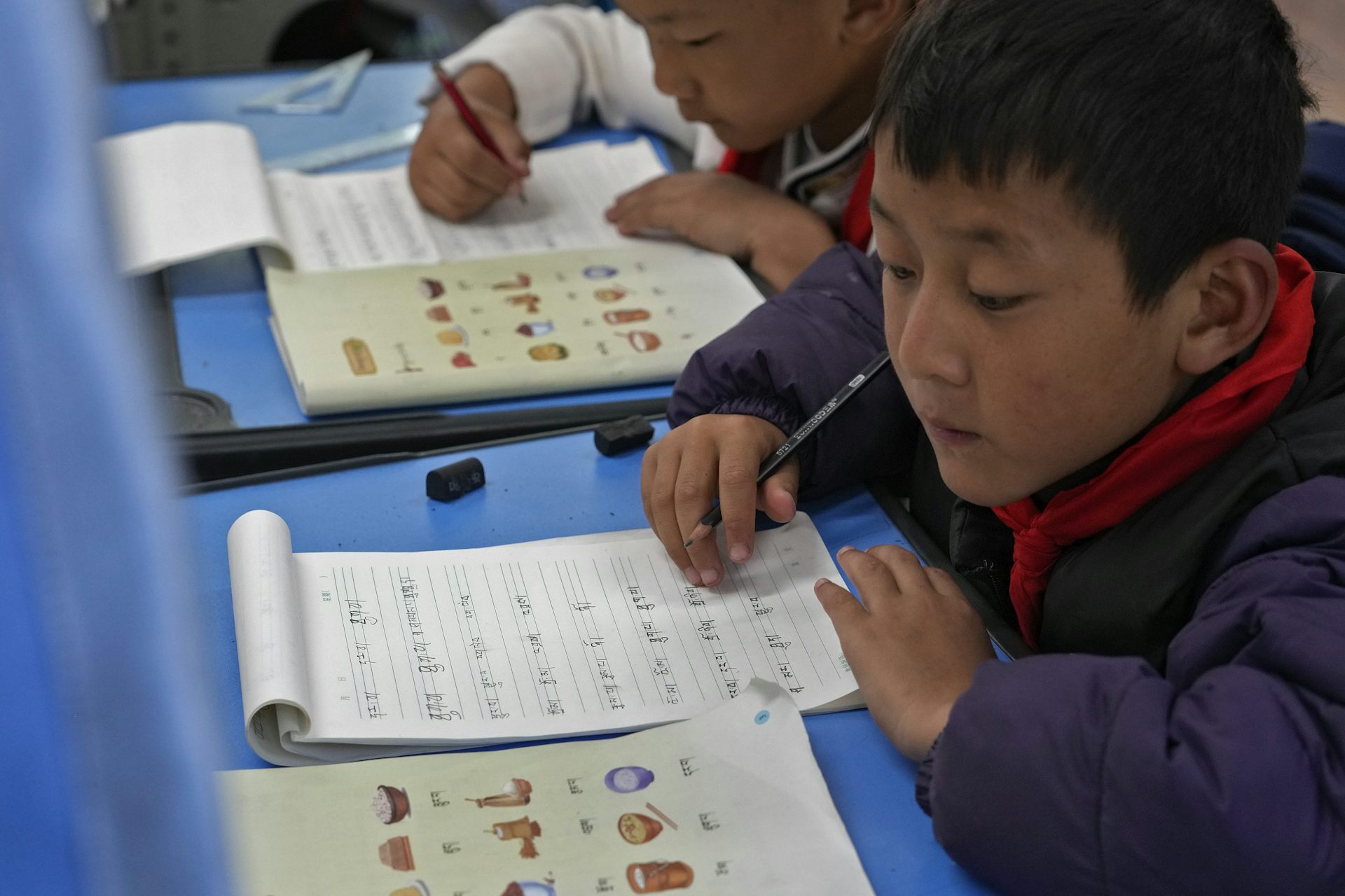 A young boy writes in a notebook in a classroom.
