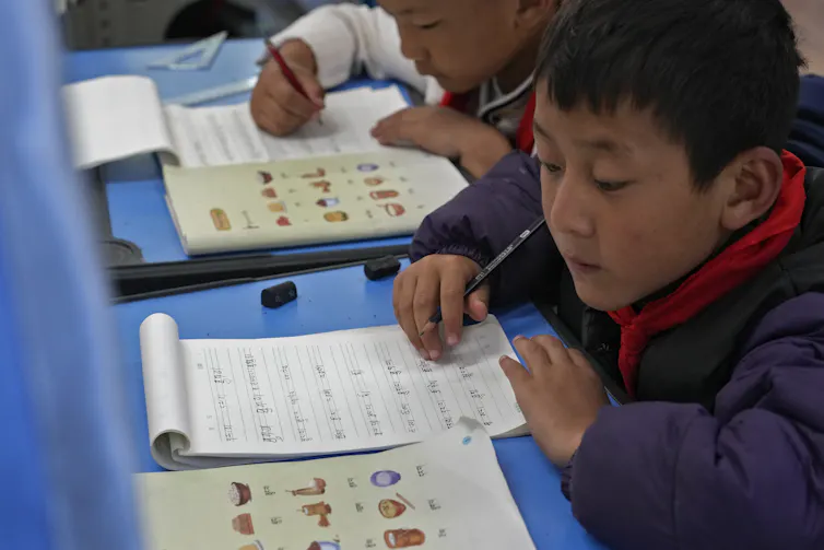 A young boy writes in a notebook in a classroom.