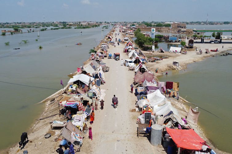 Dozens of tents line a road with floodwater on both sides.