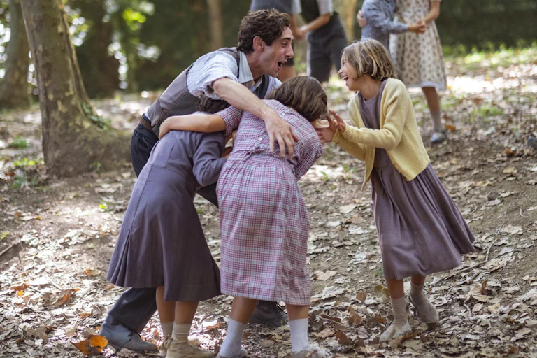 Un chico joven con chaleco juega con tres niñas en el bosque.