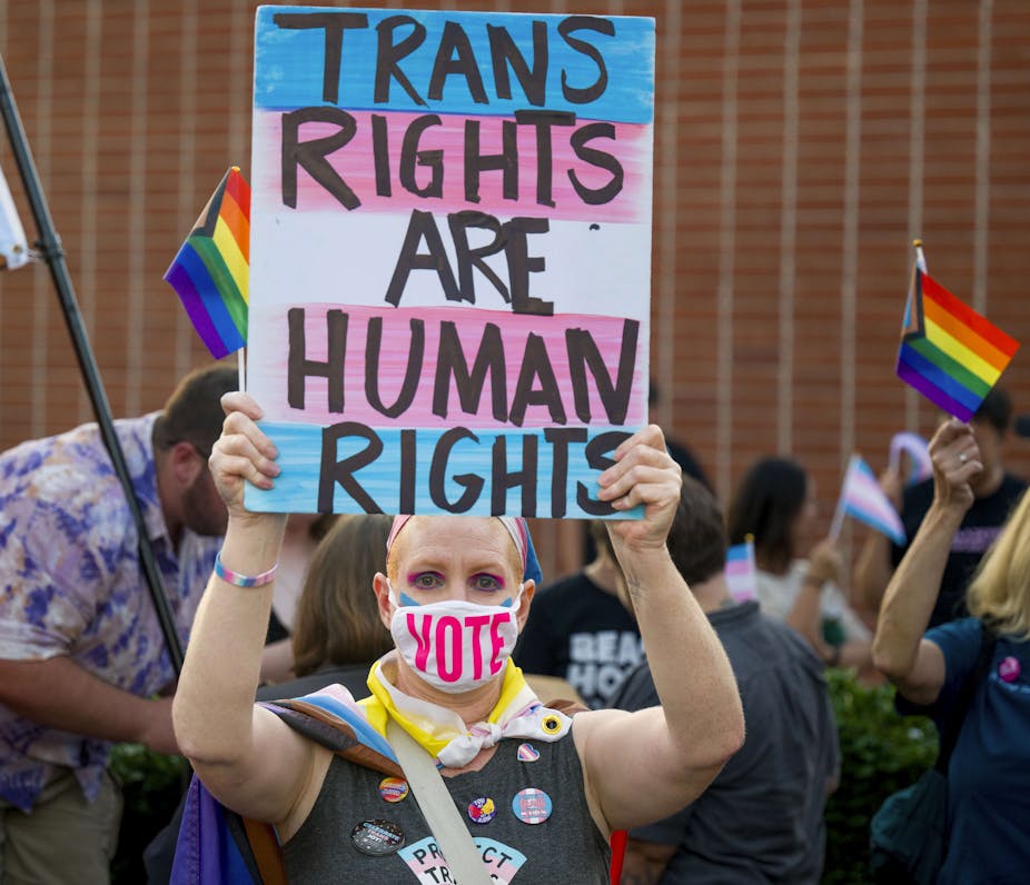 A woman wearing a mask holds up a sign that says trans rights are human rights.
