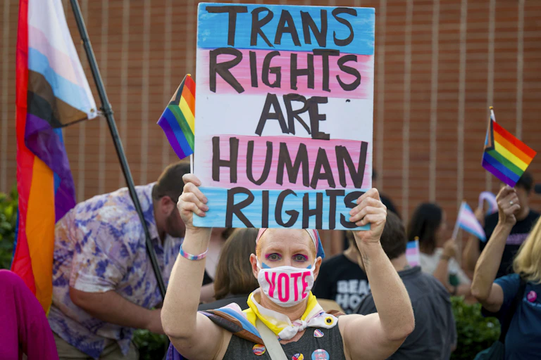 A woman wearing a mask holds up a sign that says trans rights are human rights.