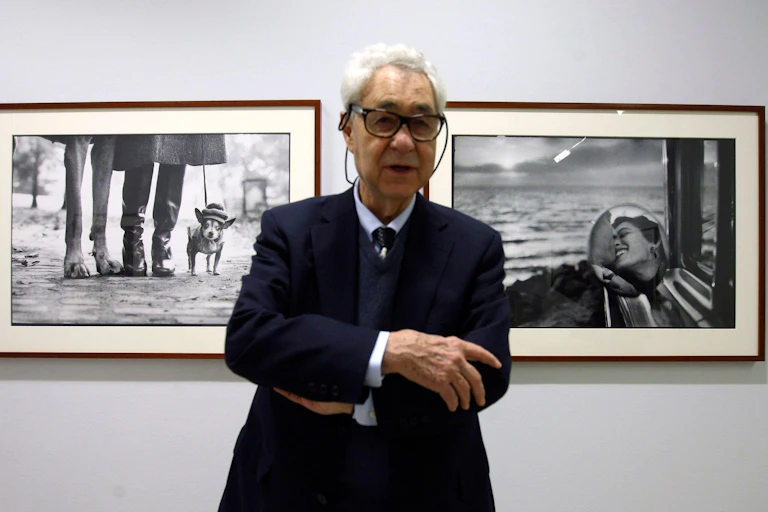 An old man with glasses (Elliott Erwitt) standing in front of two black and white photographs.