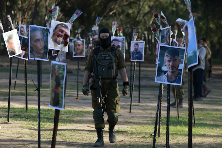Un soldat en treillis et en cagoule marche entre des dizaines de photos affichées chacune sur un bâton en bois planté dans le sol