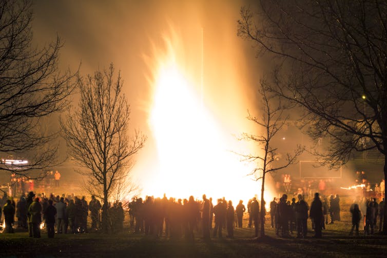 A large number of people gathered around a big bonfire in the woods.