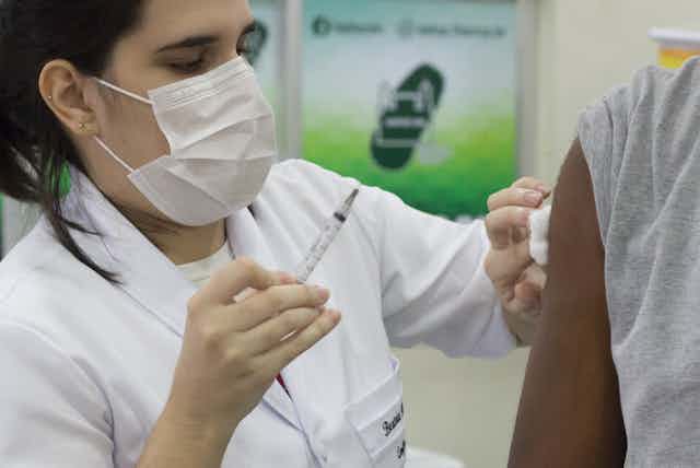 Profissional da saúde mulher segura seringa para aplicar vacina em homem negro