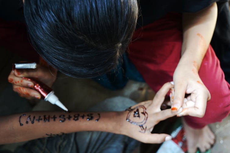 A girl decorating her friend's arm with henna.