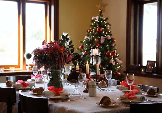A table set for a holiday dinner with a decorated Christmas tree visible in the background