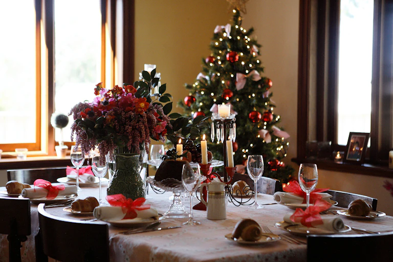 A table set for a holiday dinner with a decorated Christmas tree visible in the background