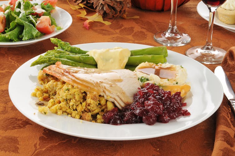 A white plate with sliced turkey, stuffing, asparagus and cranberry sauce on it