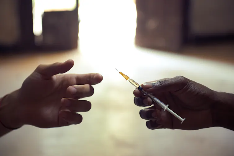 One hand passing a syringe to another.