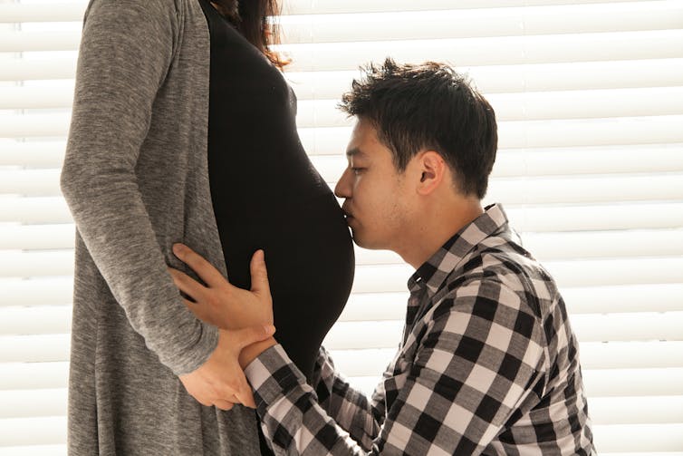 Man kisses pregnant wife's belly.