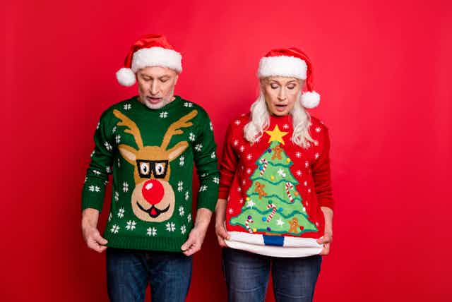 Two people wearing santa hats, looking down at their christmas jumpers.