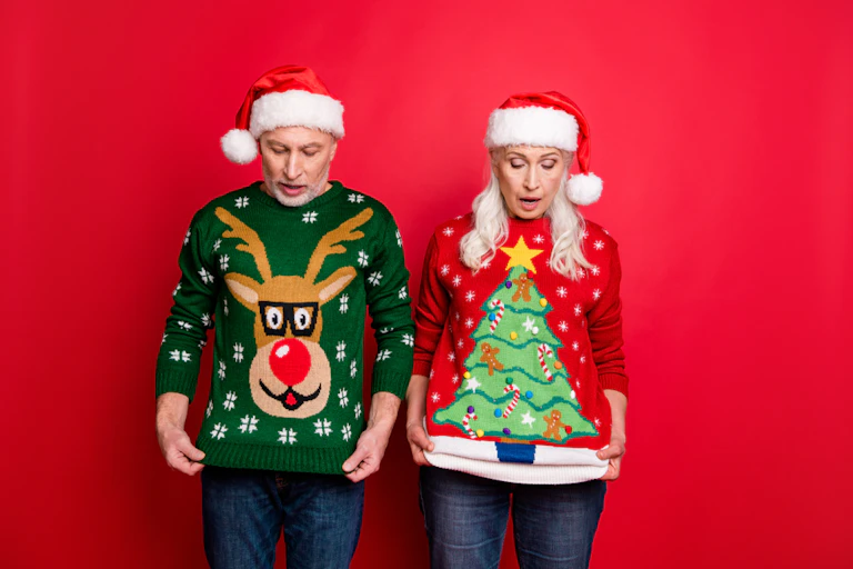 Two people wearing santa hats, looking down at their christmas jumpers.