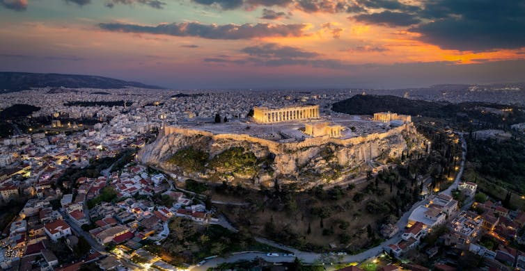 View of the Parthenon temple and the old town of Plaka at dusk surrounded by city of Athens.