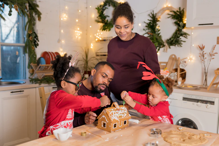 A family decorates a gingerbread house.