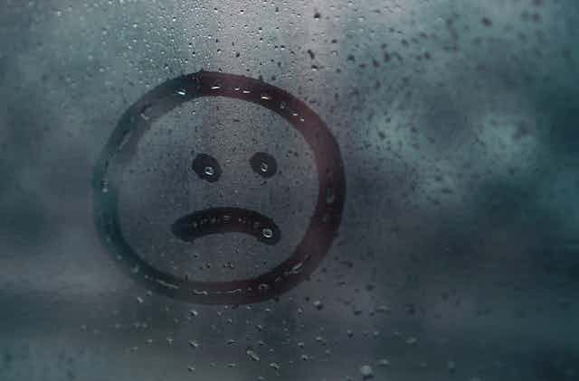 Sad face drawn in condensation on window