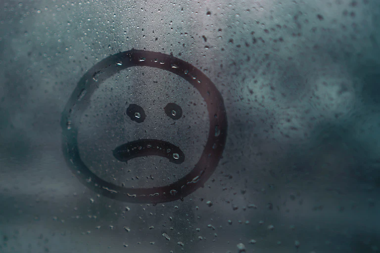 Sad face drawn in condensation on window
