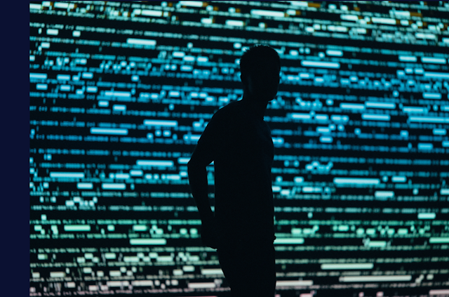 La silhouette d'un homme en contrejour devant un mur d'écran lumineux et strié de lumière verte et bleue.