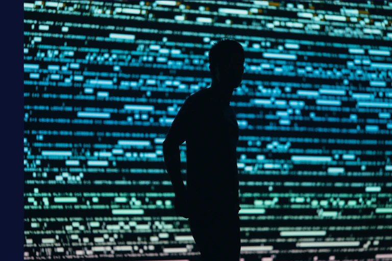 La silhouette d'un homme en contrejour devant un mur d'écran lumineux et strié de lumière verte et bleue.