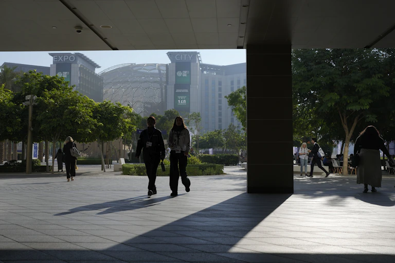 Two people in shadow seen walking towards the camera in front of a large building.