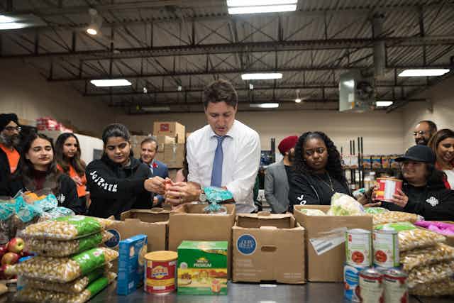 the PM stands in front of food and boxes with women to his right.