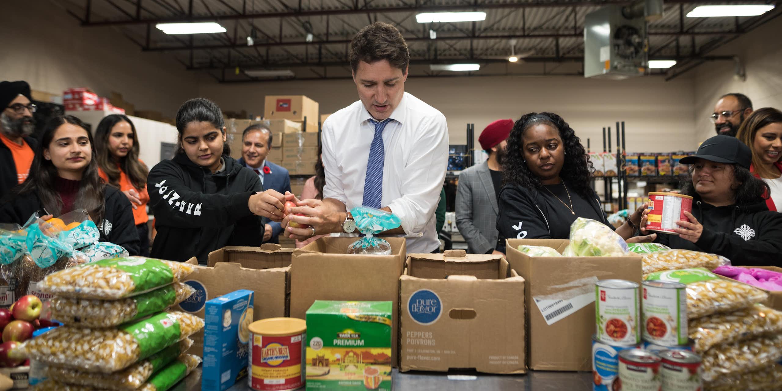 the PM stands in front of food and boxes with women to his right.