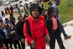 A Black woman wearing a bright red outfit climbs a set of exterior stairs