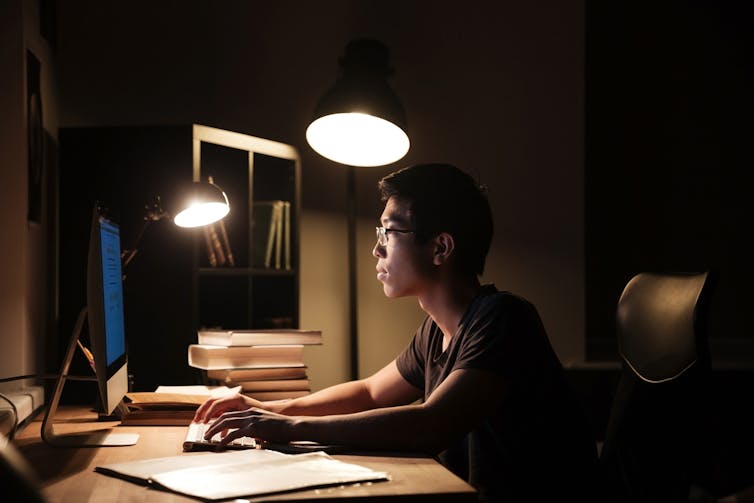 A young Asian man looks at a computer at night time.