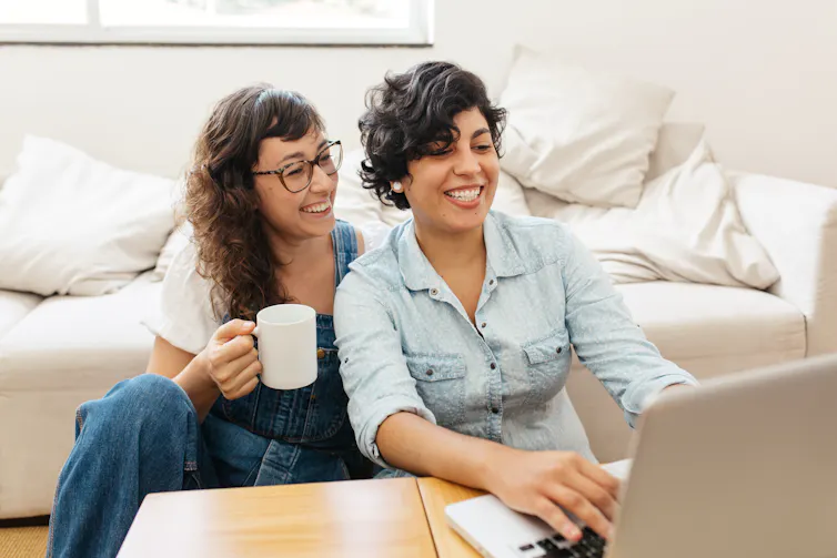 two young woman sitting on the floor, working on a laptop.