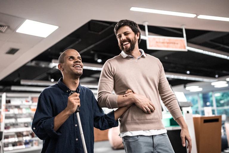 vision impaired man walks holding arm of another man in supermarket