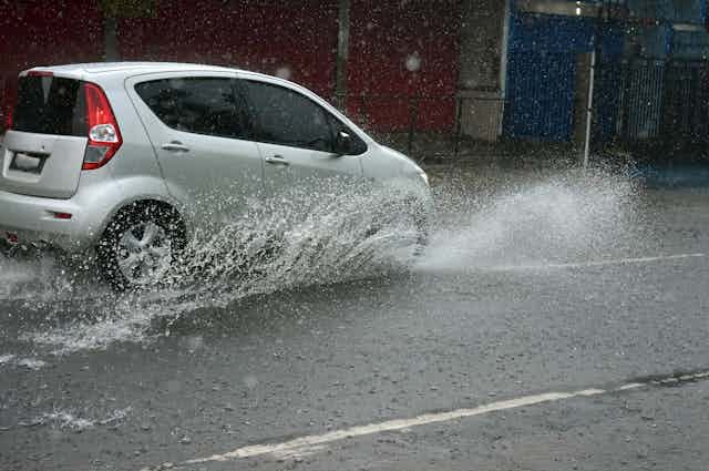 A small white car drives through stormwater on a road